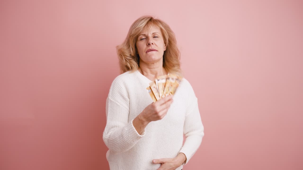 Donna felice che tiene in mano un ventaglio di banconote su sfondo rosa