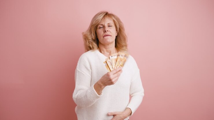Donna felice che tiene in mano un ventaglio di banconote su sfondo rosa