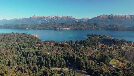 aerial view of a forest with houses, a lake and the andes mountains in the background