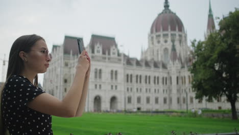 young woman taking photo of the hungarian parliament building