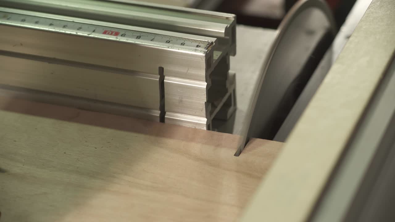 A close-up of a table circular saw blade cutting a small piece from a plywood board at a right angle