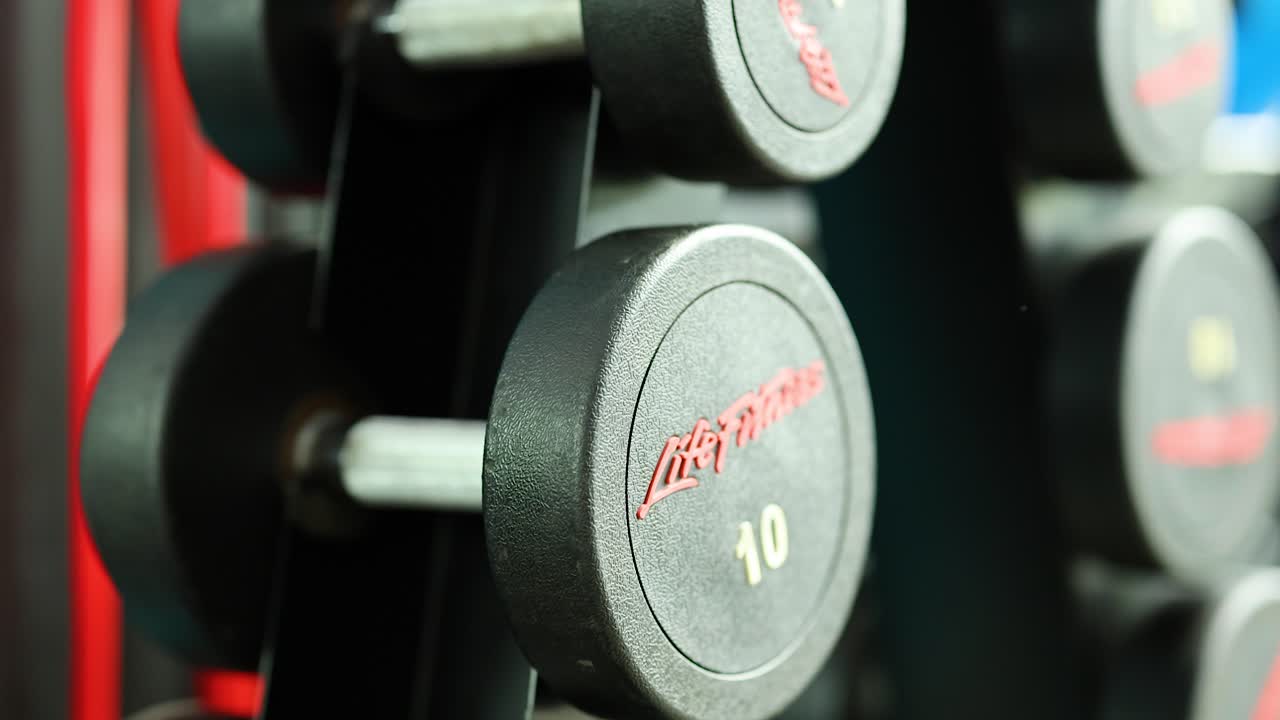 Close-up view of a dumbbell rack in a well-lit gym, showcasing various weights and vibrant background colors