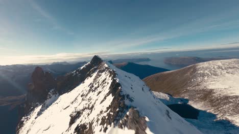 vuelo fpv a lo largo de los picos nevados de la cordillera en noruega durante el frío día de invierno con luz solar - océano en segundo plano