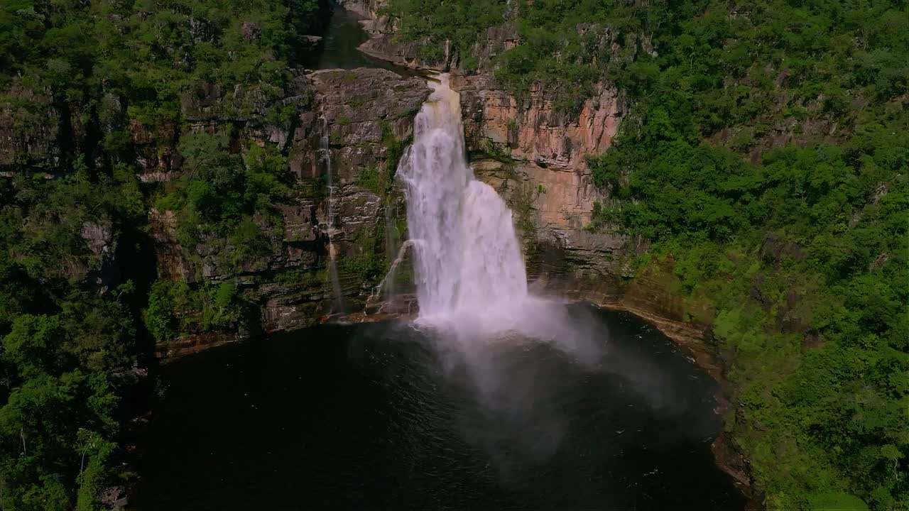 Aerial view of stunning waterfall plunging into a dark pond, in Chapada Dos Veadeiros National Park, showcasing the raw beauty of Brazilian nature, slow motion static shot
