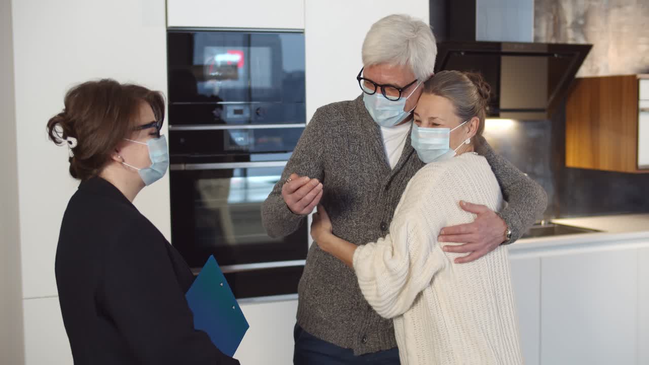 여성 부동산 대리인과 함께 새로운 집에 서 있는 의료 마스크를 입은 행복한 부부입니다.