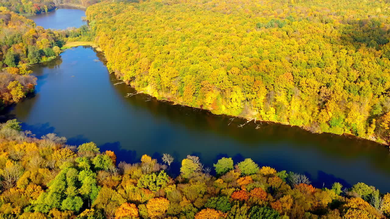 Wonderful scenery of green and yellow woods in autumn season. Calm water flowing in the river through the forest. Aerial view.