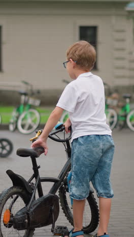 se ve a un niño joven por detrás, corriendo emocionado hacia una bicicleta negra estacionada, en el fondo, varias bicicletas están alineadas, con un hombre de pie cerca y otro niño montando una bicicleta