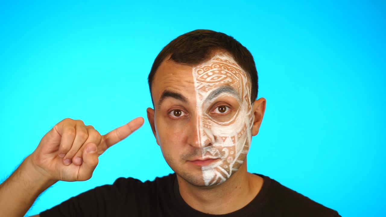 el hombre con la cara pintada está gestando sus dedos contra los templos, ¿estás loco, sobre un fondo azul?