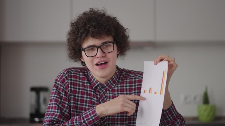 A man with glasses looking at the camera shows a graph