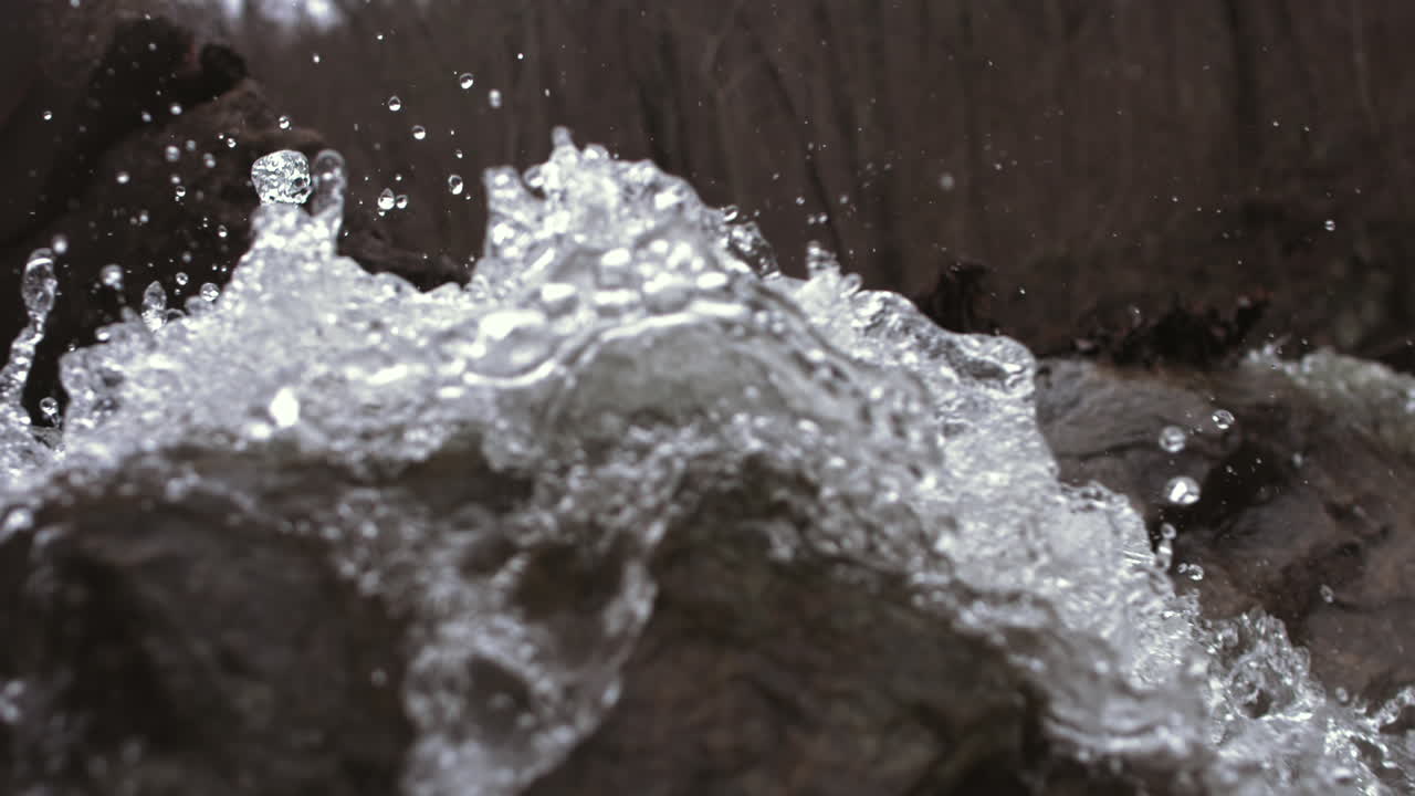 Super slow motion footage of water hitting a rock and rolling off of it in big droplets.