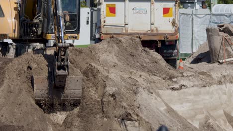excavator loads soil into dump truck on sunny construction site, wide shot, natural daylight