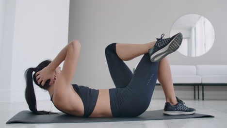 mujer morena caucásica haciendo ejercicio abdominal mientras está acostada en una alfombra. ejercicios diarios en casa para un cuerpo saludable.