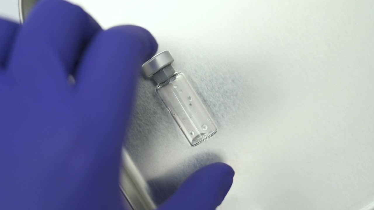 Medical professional taking an empty glass vial from a stainless steel tray in a laboratory setting