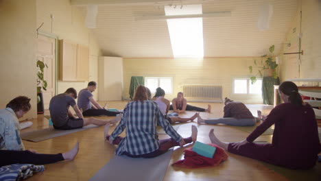 yogis sit with legs out stretching in group yoga class led by instructor