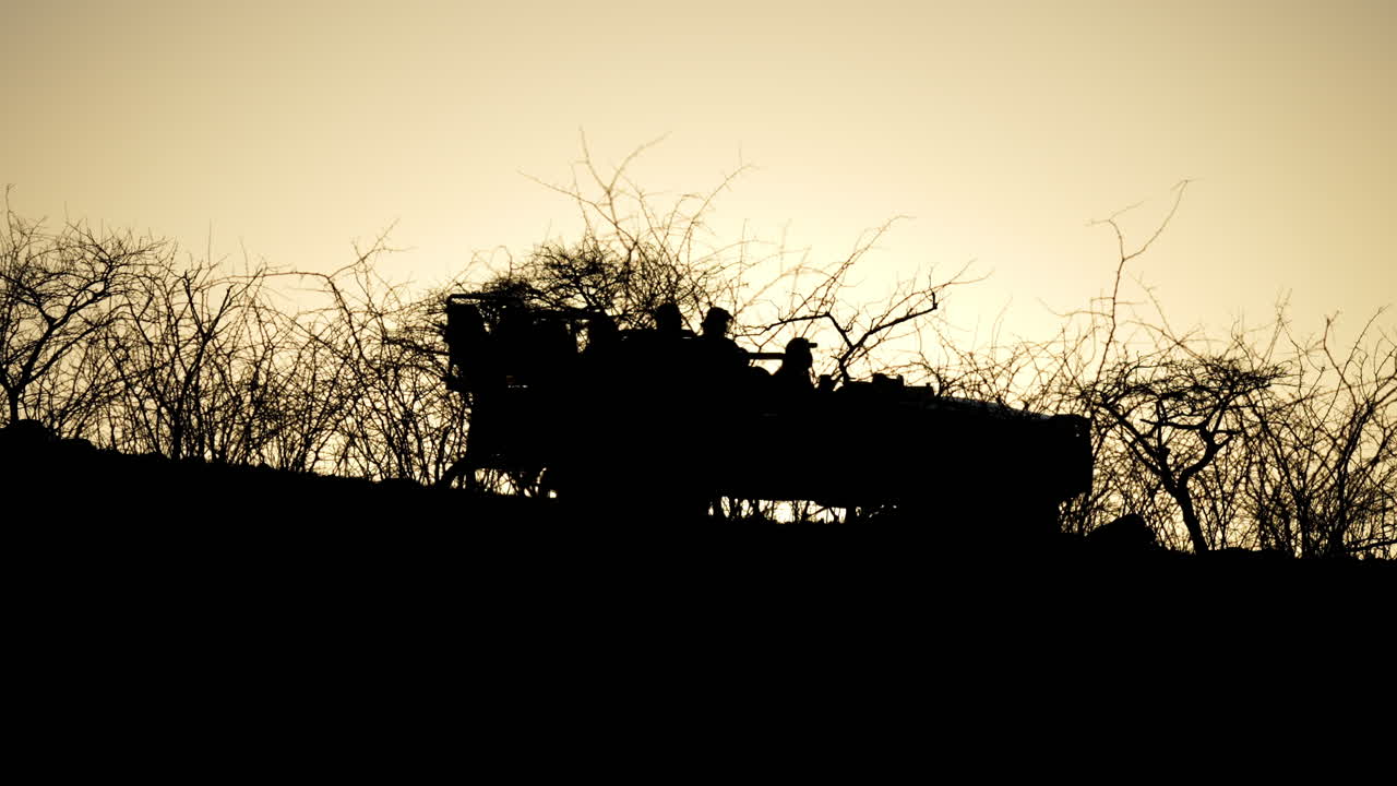 일출이나 일몰의 황금빛 빛이 정적인 장면으로 아프리카 덤불을 가로질러 여행하는 사파리 차량 실루엣
