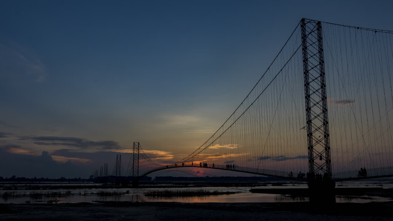 태양이 배경에 지는 찬다니 도다라 현수교의 저녁 시간 경과와 네팔 서부 카르날리 강을 건너는 사람들