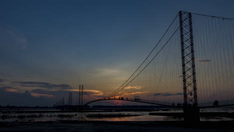 timelapse vespertino del puente colgante chandani dodhara con la puesta de sol en el fondo y la gente cruzando el puente sobre el río karnali, oeste de nepal