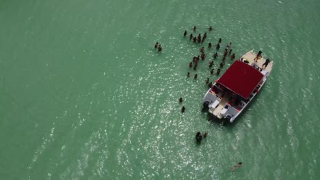 drone flies over a tourist boat in the sea where people are standing in the turquoise sea enjoying the water