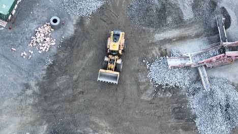 Drone-shot-Tracking-Mining-Bob-Cat-Truck-as-it-moves-around-quarry,-preparing-to-collect-rocks-from-conveyer-belt