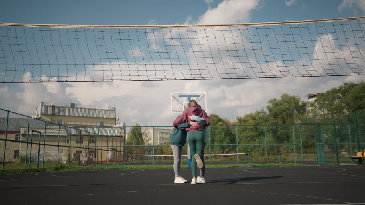 젊은이들이 푸른 야외 볼리볼 코트, 배경에 건물, 경기장에서 스포츠 시설, 밝은 낮에 야외에서 팀 활동을 즐기는 활발한 사람들의 그룹에서 행복하게 함께합니다.