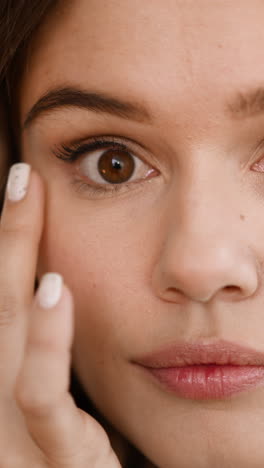 focused woman smears concealer on soft skin under eyes to cover flaws. redhead lady prepares for evening makeup on blurred background closeup