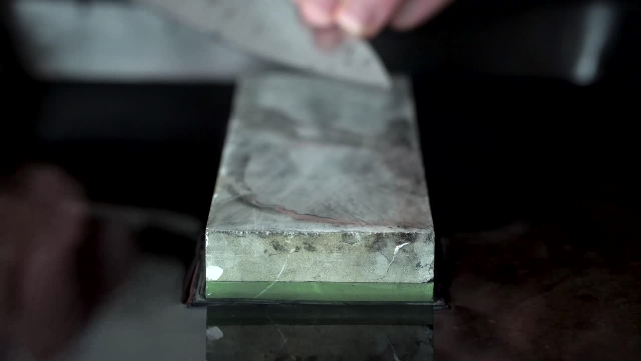 manos masculinas afilando cuchillos de chefs japoneses usando piedra de afilar