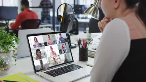 mujer caucásica teniendo una videoconferencia con colegas de oficina en una computadora portátil en la oficina