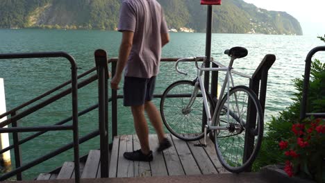 guy reaches his destination and leaves his bike open on the deck nearby a lake to go to on adventures