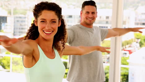 pareja feliz y en forma sonriendo a la cámara haciendo yoga