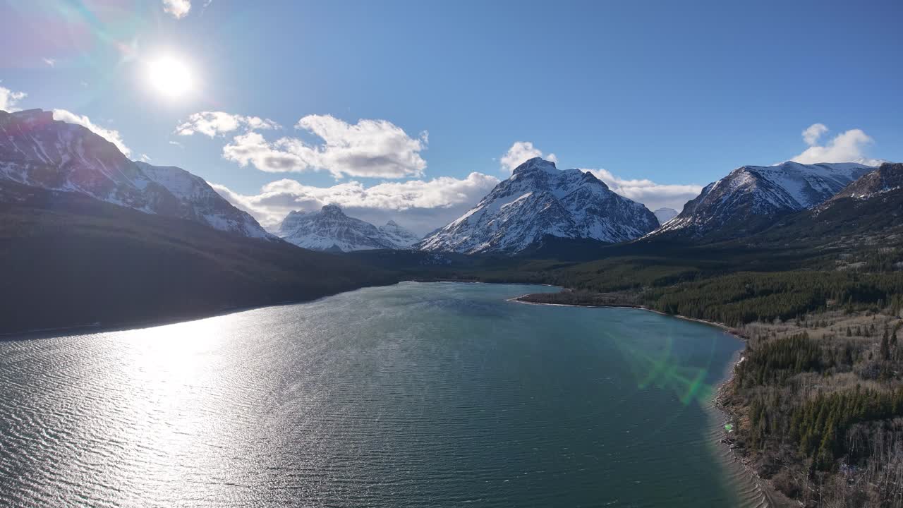 Veduta aerea con drone di un lago scintillante con riva boscosa e montagne innevate sotto un sole splendente in Montana