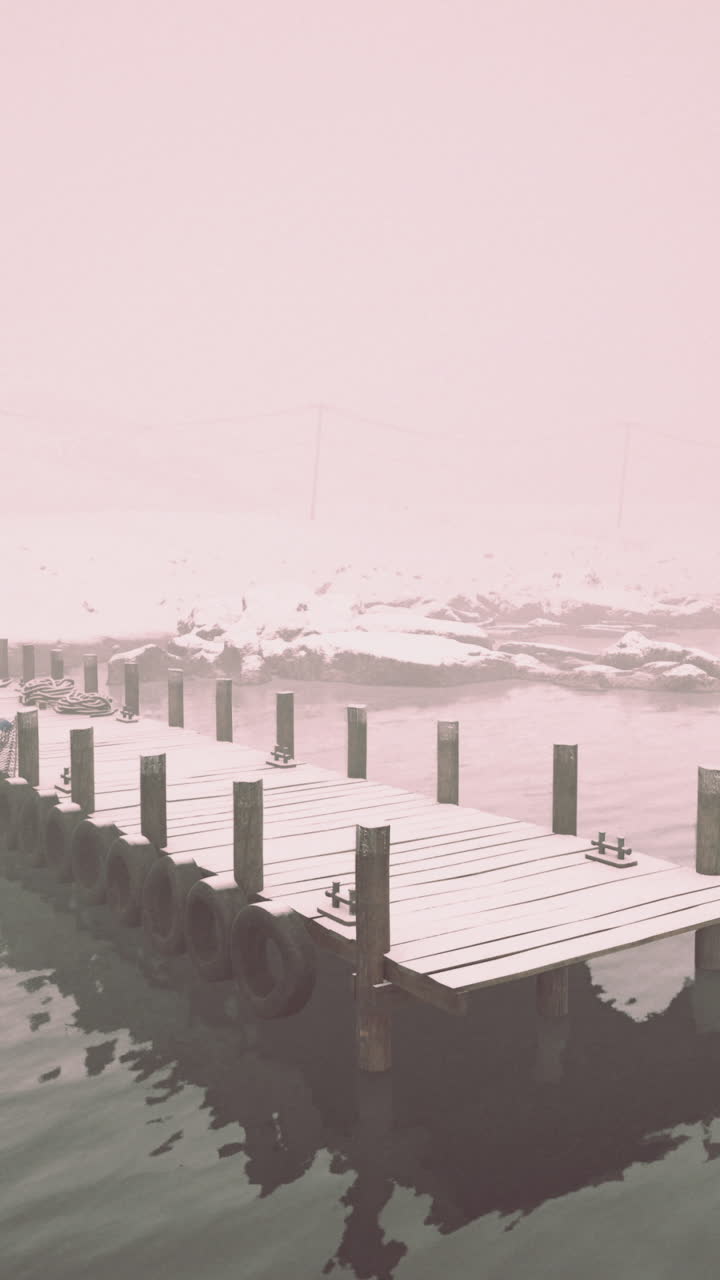 A snowy wooden dock stretches out into a foggy lake