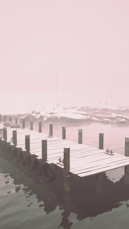 a snowy wooden dock stretches out into a foggy lake