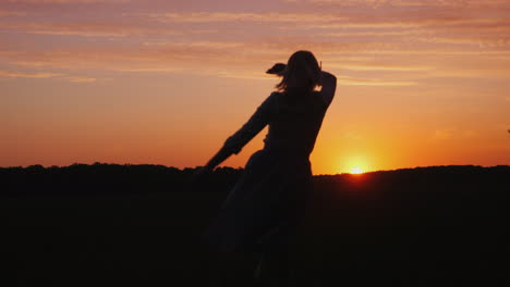 Silueta-De-Una-Mujer-Despreocupada-Con-Un-Vestido-Ligero-Corre-Por-El-Campo-Hacia-La-Atardecer-4k-Vid