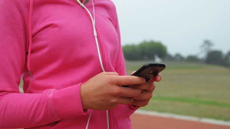 Sección-Media-De-Una-Atleta-Femenina-Usando-Un-Teléfono-Móvil-En-Un-Recinto-Deportivo-4k