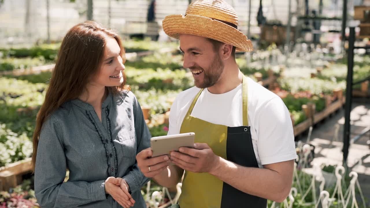 Red-haired girl approaches a gardener with a tablet in the Greenhouse