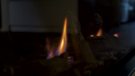 slow motion close-up landscape view of gas fireplace flames burning fake wooden logs charcoal ash household heater indoor modern design glass panel