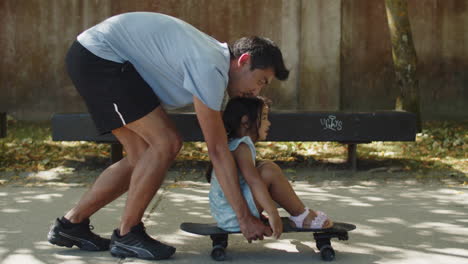 padre joven feliz moviendo patineta con su pequeña hija