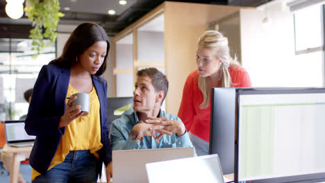happy diverse male and female colleagues using computers in discussion at desk, slow motion