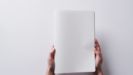 Close-up-of-hands-holding-book-with-copy-space-on-white-background-in-slow-motion