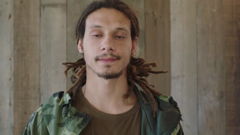 portrait of young mixed race man dreadlocks hairstyle looking serious at camera confident male wearing camouflage jacket wooden background