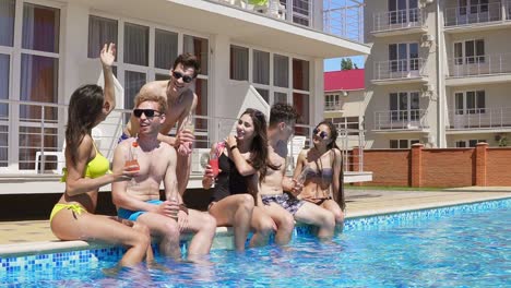 glückliche gruppe junger freunde, die im sommer mit cocktails abhängen und am rand des pools plaudern 1