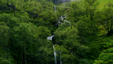 toma aérea de drones de un arroyo cuesta abajo y una cascada en glen coe