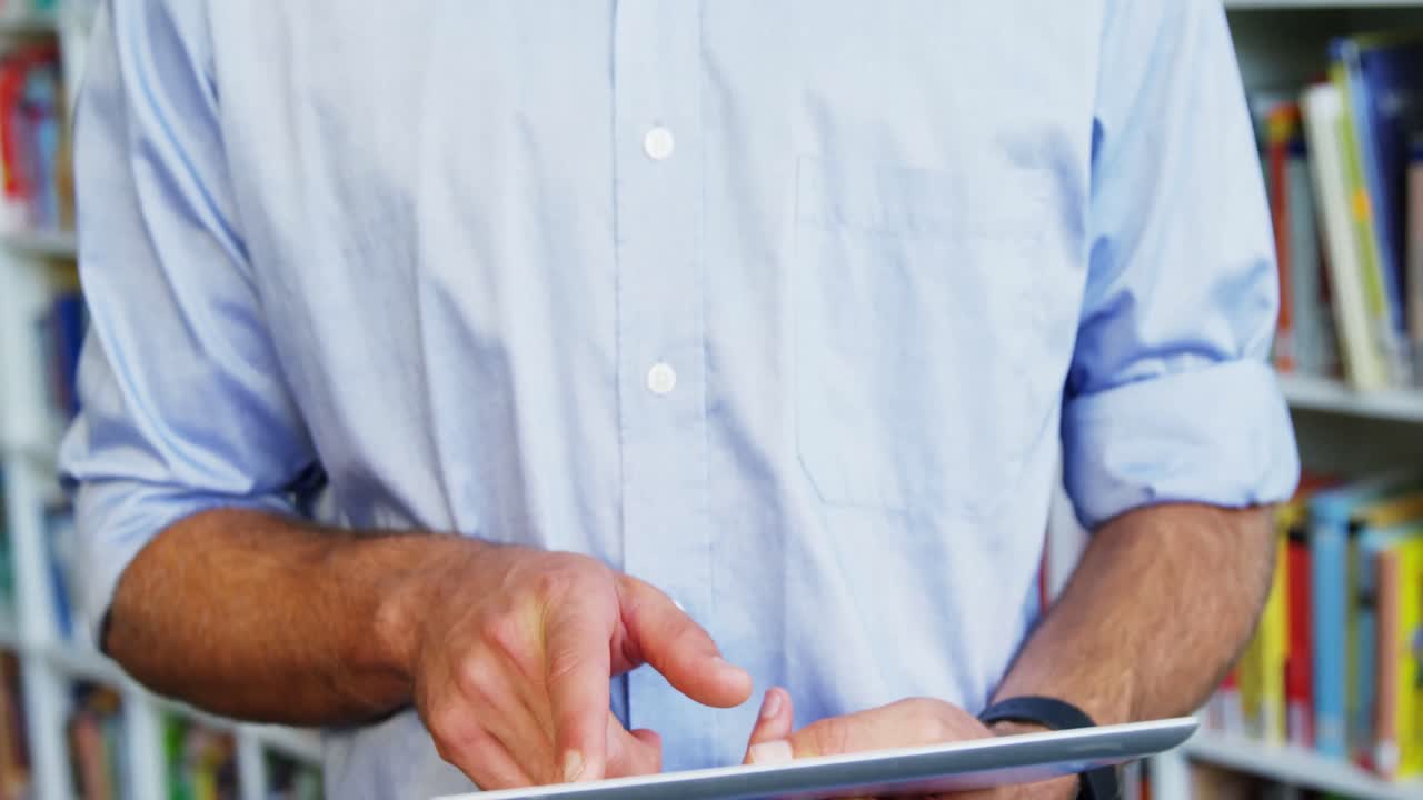 sección media de un maestro de escuela usando una tableta digital en la biblioteca de la escuela