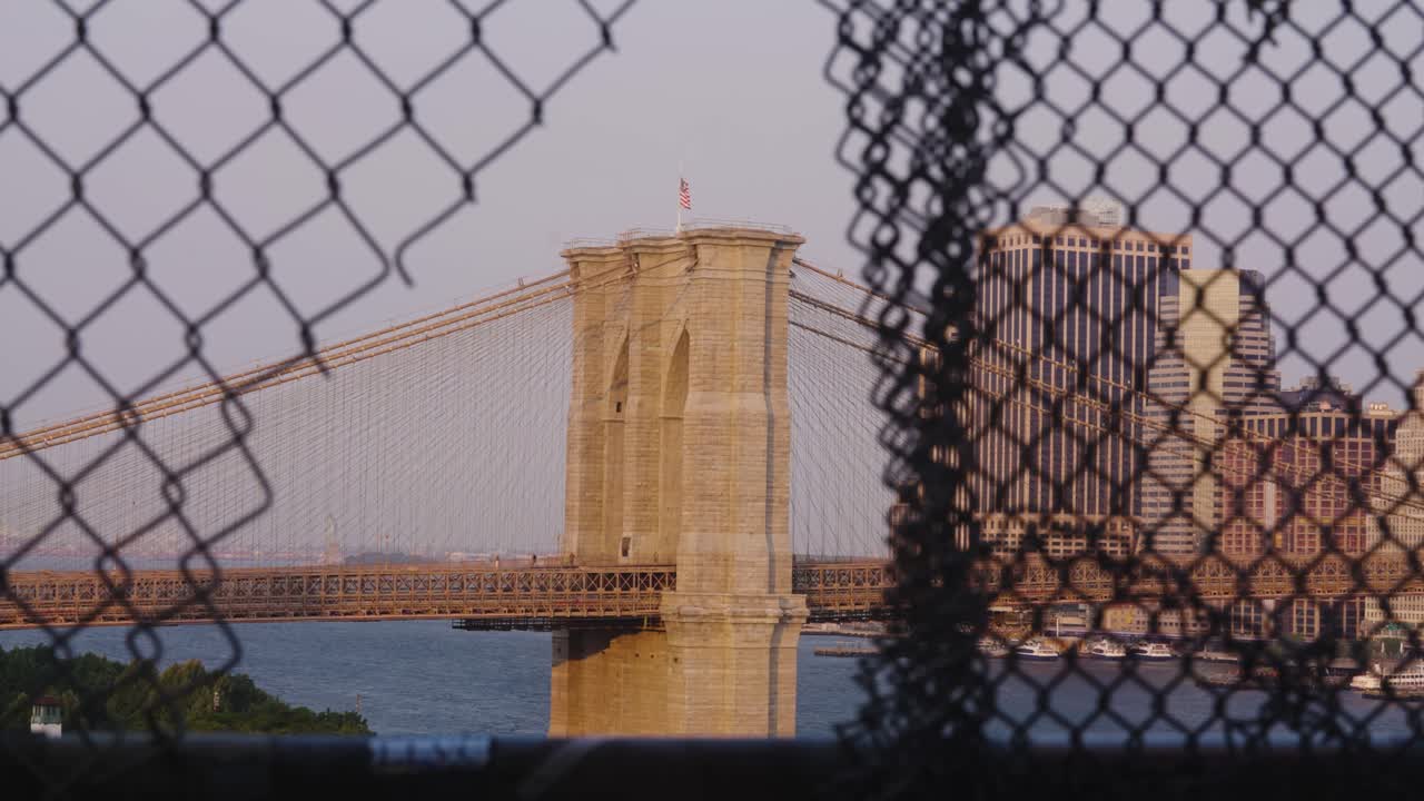 Bandiera americana che sventola sul Ponte di Brooklyn a New York durante l'ora d'oro - Ripresa dal Ponte di Manhattan attraverso la recinzione