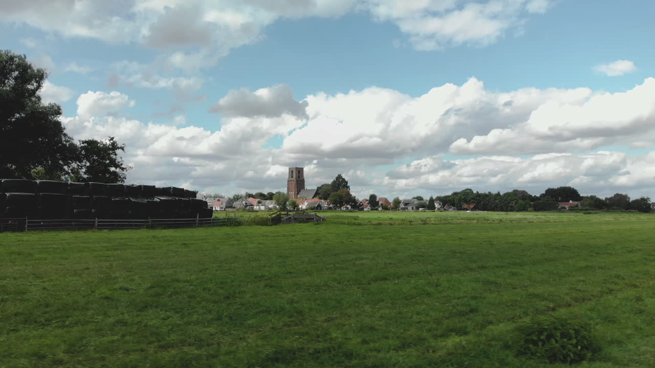 구름과 새가 지나가는 푸른 하늘을 배경으로 네덜란드 암스테르담 근처의 란스도르프 마을 밖에 있는 패스트리 밭을 가로지르는 낮은 공중 팬