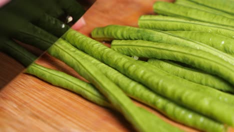 Macro-cutting-Thai-beans-in-half-with-a-black-knife-on-a-wooden-cutting-board