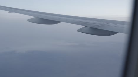 Aerial view from airplane window, wing over clouds at high altitude, tranquil sky