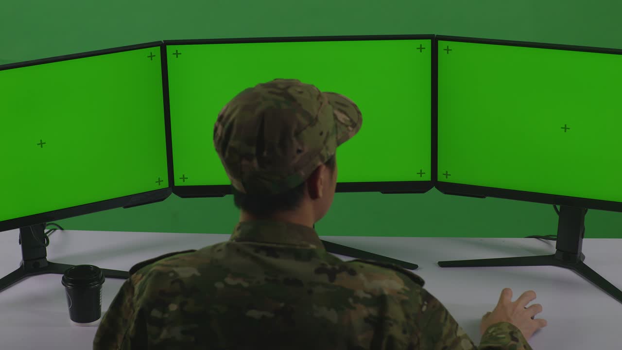 vista trasera de un soldado asiático trabajando con un simulacro de varios monitores de computadora en un estudio de pantalla verde