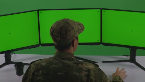 녹색 스크린 스튜디오에서 여러 컴퓨터 모니터를 모의로 작업하는 아시아 남성 군인의 뒷면