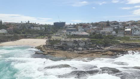 Olas-Peligrosas-Sobre-La-Costa-Rocosa-Con-Surfistas-En-El-Cabo-De-Tamarama-Point-En-Los-Suburbios-Del-Este,-Sydney,-Nueva-Gales-Del-Sur,-Australia